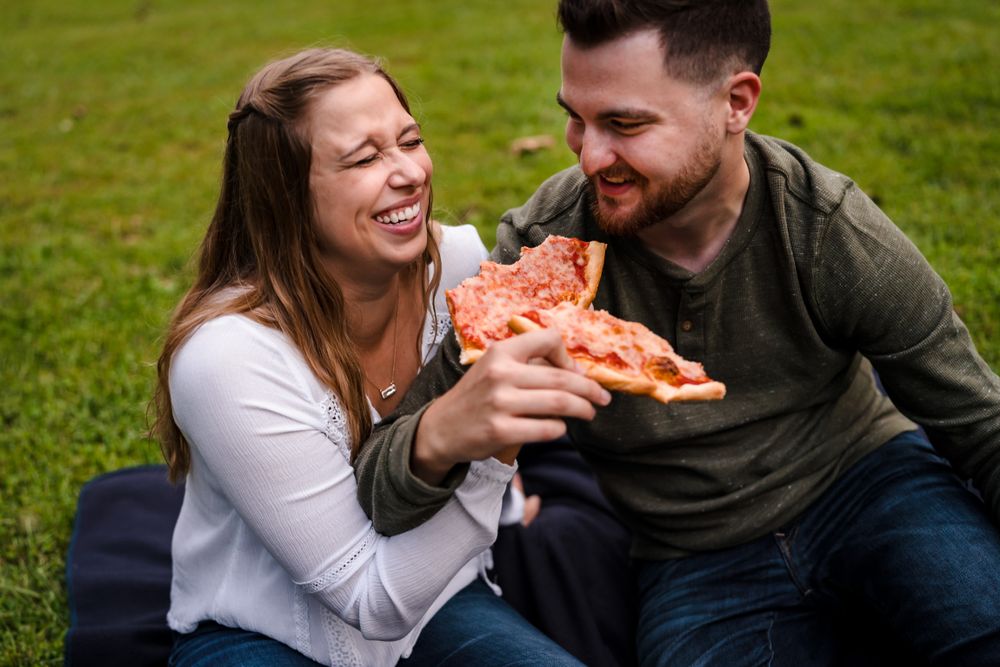 A couple shares laughter while enjoying a meal together on a grassy lawn.
