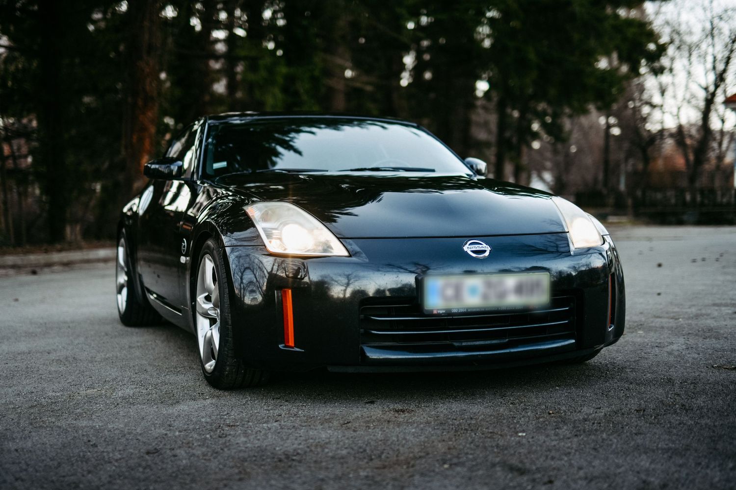 Black Nissan 350Z sports car parked on gravel with forest background.