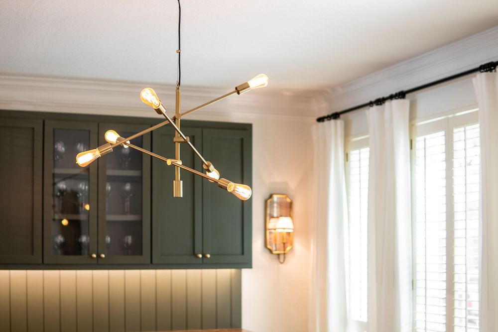 Modern brass sputnik chandelier with multiple arms illuminates a space with dark green cabinets.