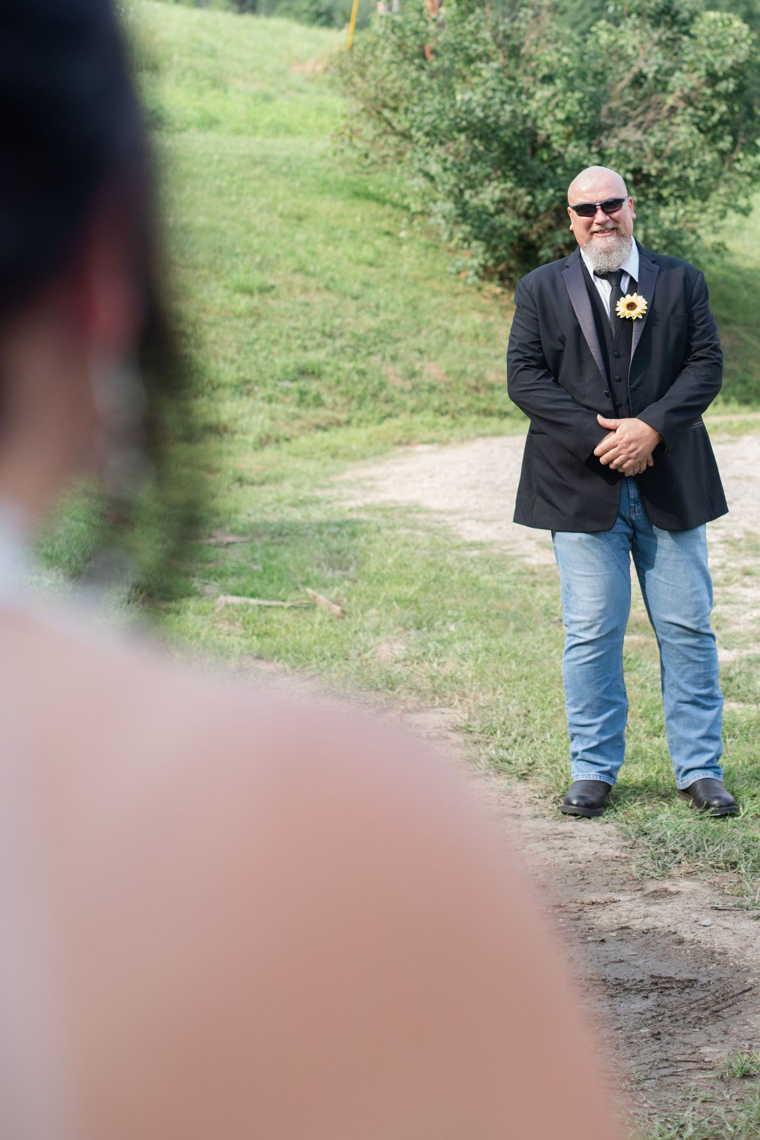 Figure in casual formal wear stands alone on a natural pathway surrounded by greenery.
