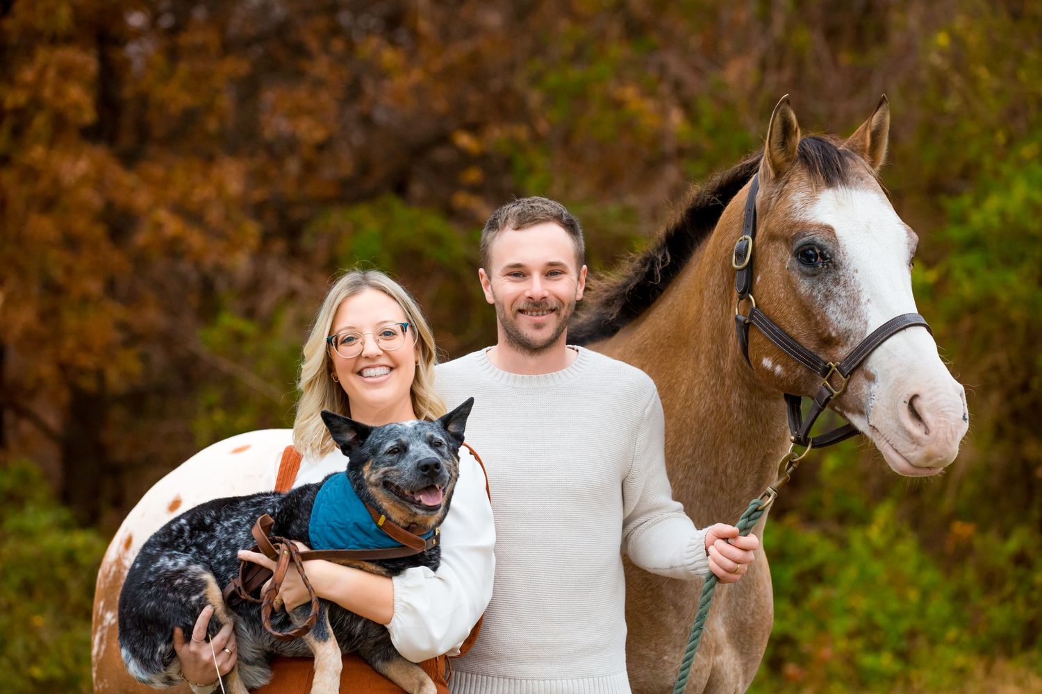Couple outdoors with their beautiful horse and australian shepherd dog against fall foliage.