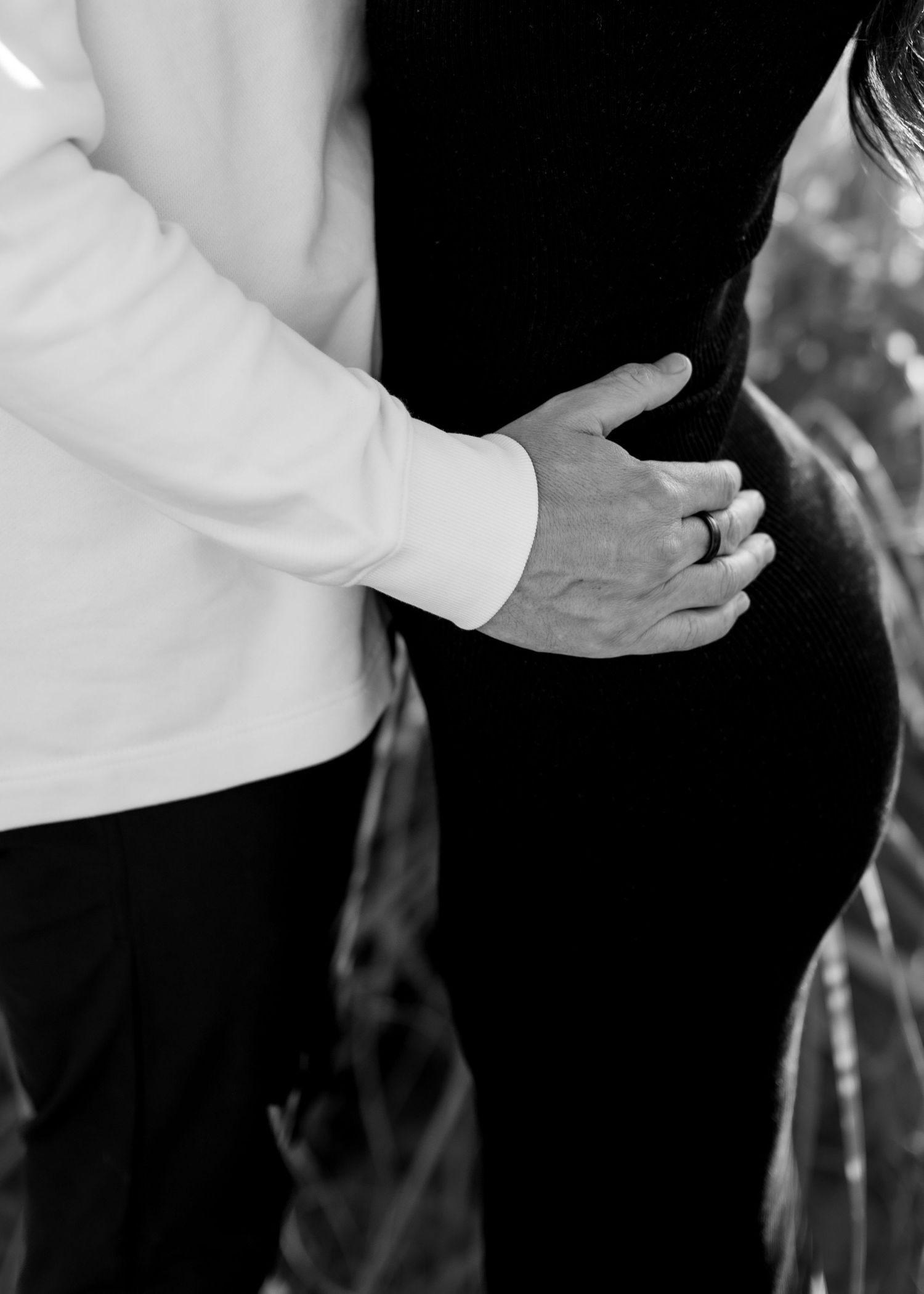 Black and white detail of formal wedding attire and clasped hands.