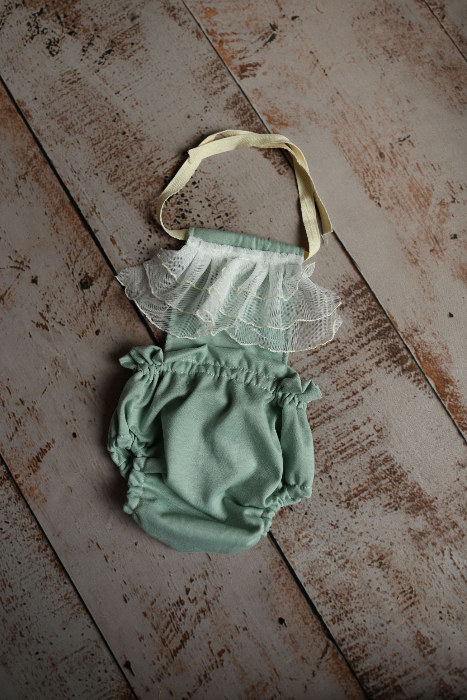 Mint green baby romper with white ruffle detail on rustic wooden background.