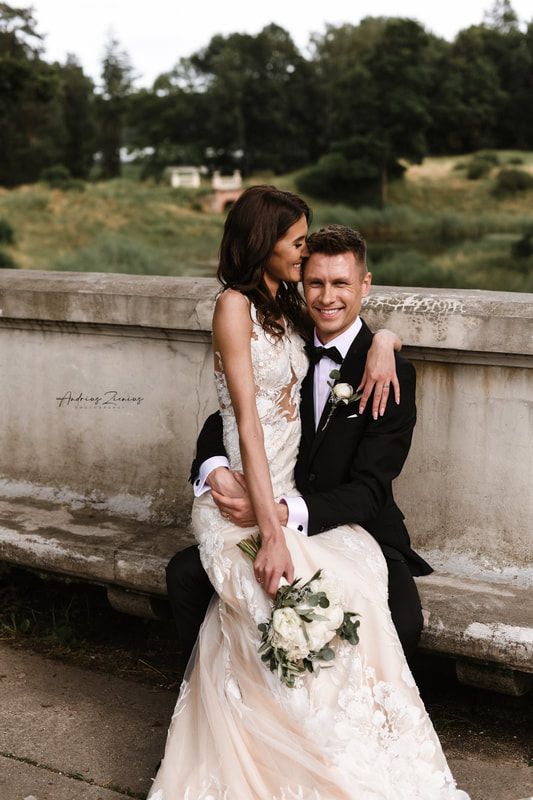 Wedding couple sitting on stone wall during outdoor photo session in natural setting.