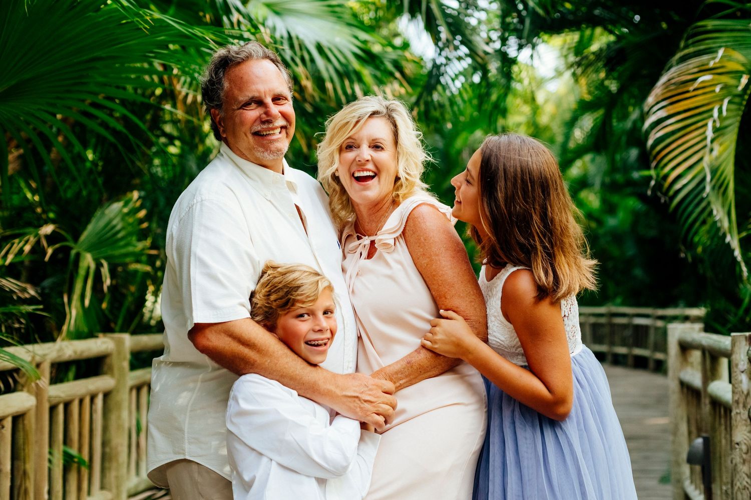 Family sharing a joyful moment together on a wooden boardwalk surrounded by tropical plants.
