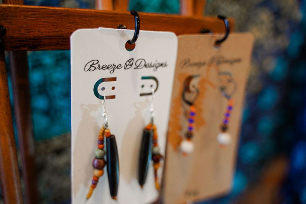 Display of handmade earrings with beaded and feather designs on wooden jewelry stands.