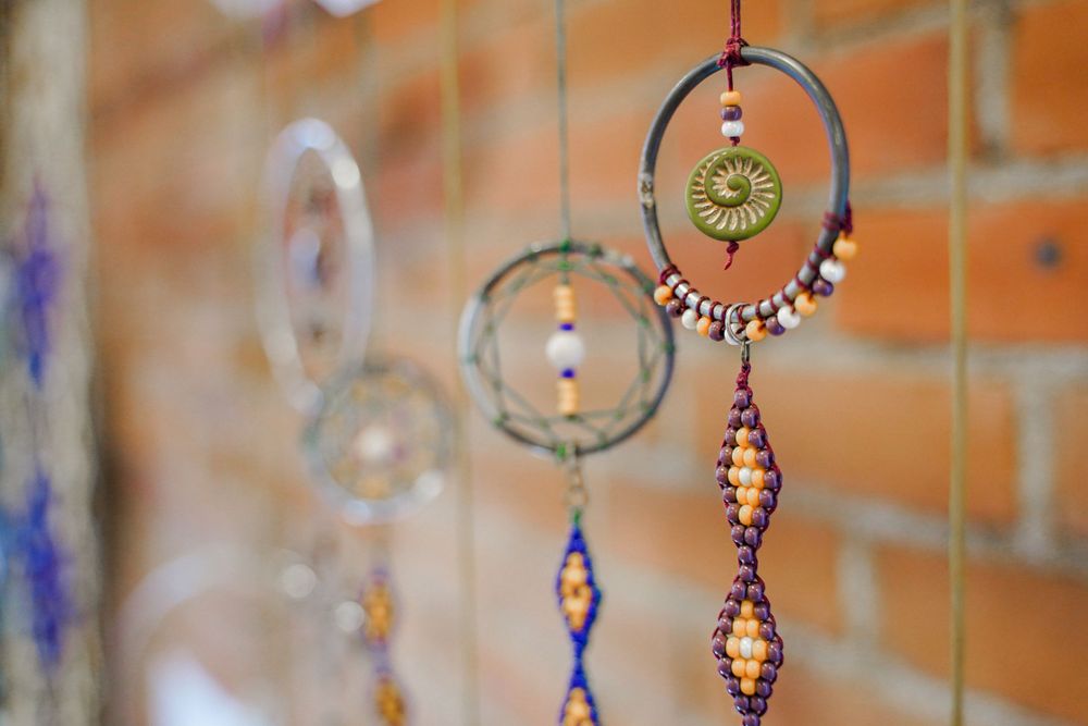 Decorative bohemian dreamcatcher with beads hanging against orange brick wall.