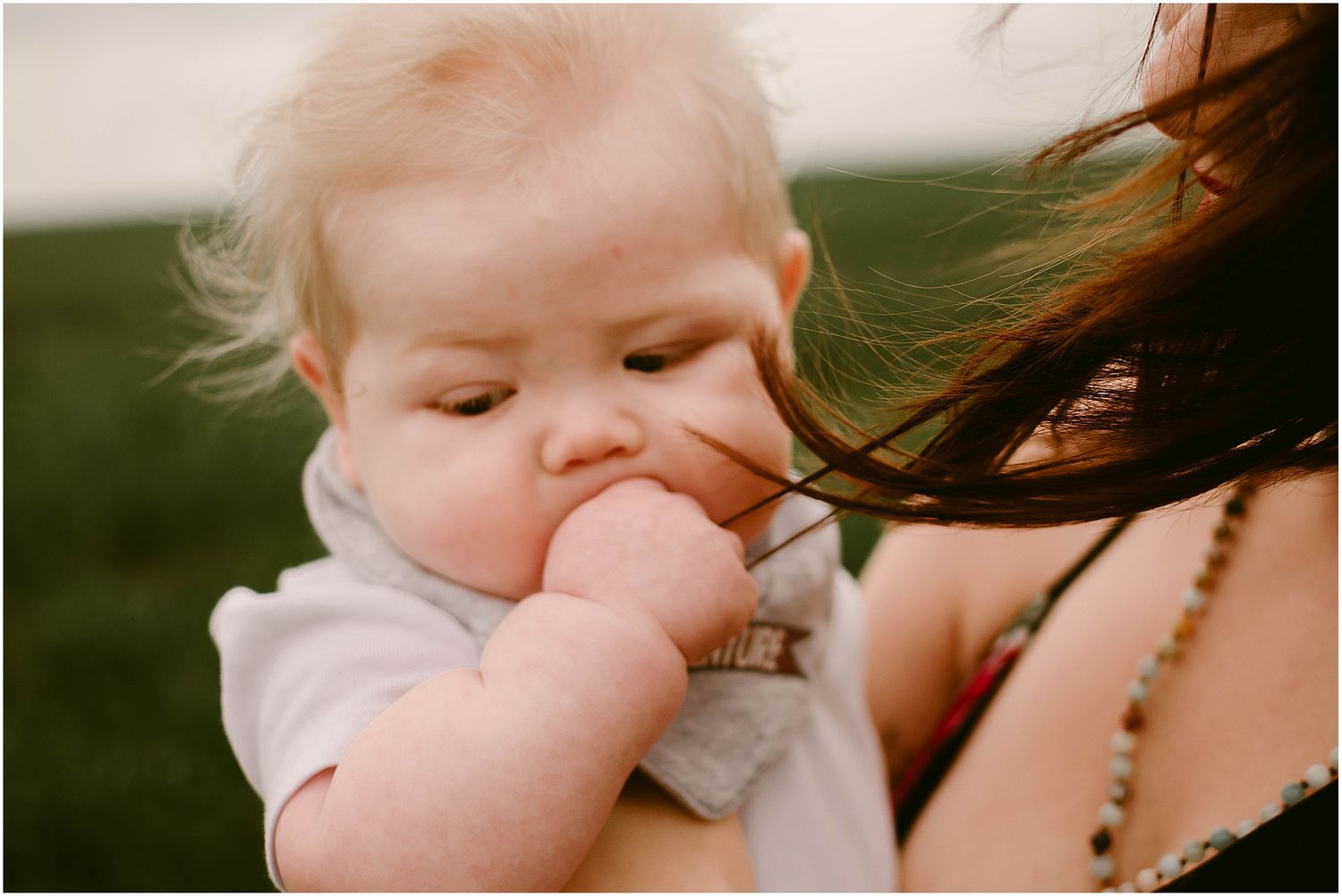 Close-up of baby in gray shirt tenderly touching parent's hair outdoors.
