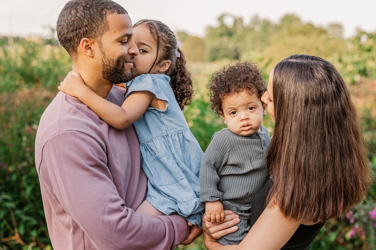 A loving family embraces outdoors in a garden setting during a warm afternoon.