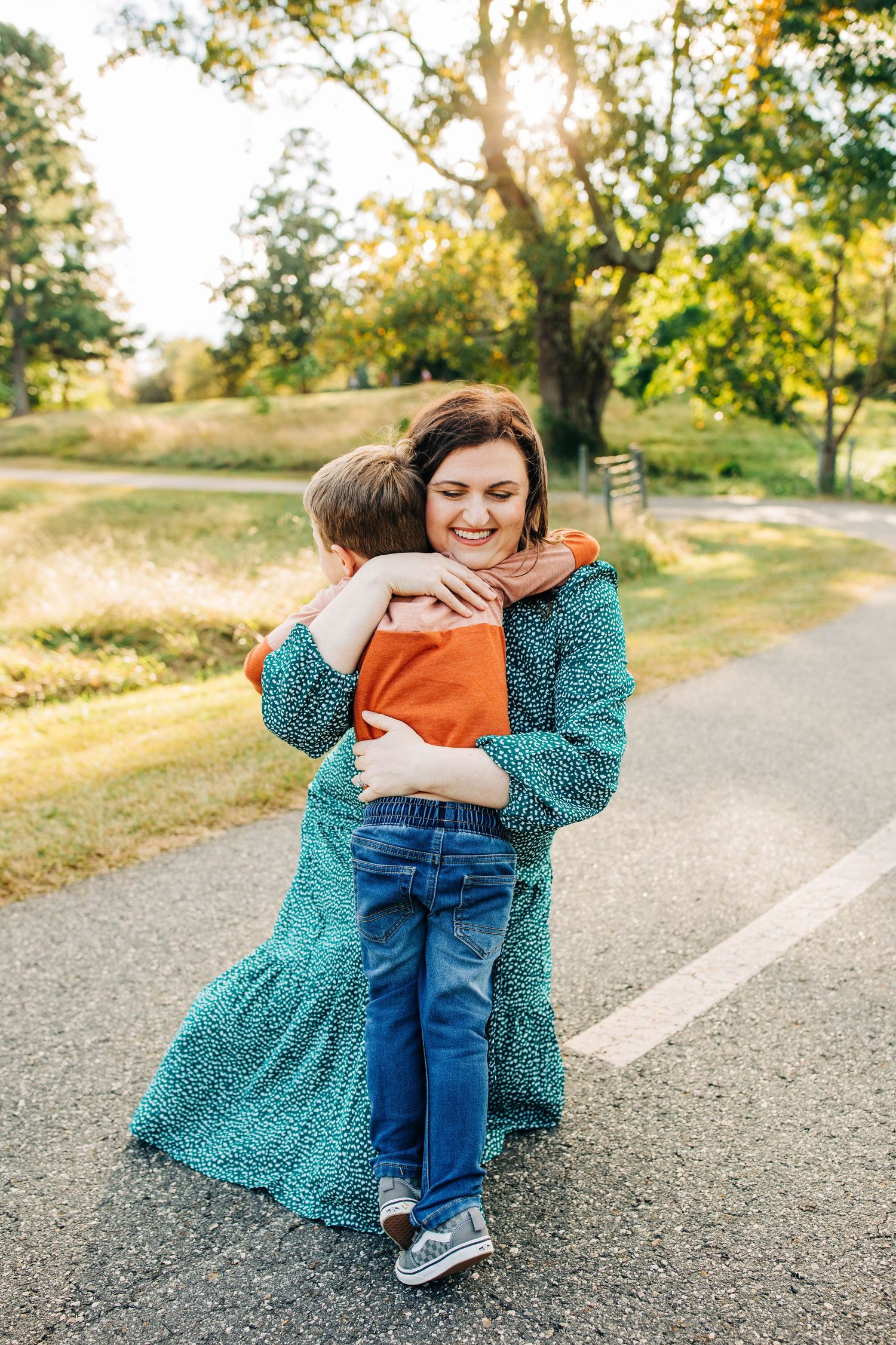 A tender embrace shared between two people on a sunny country path with golden sunlight filtering through trees.