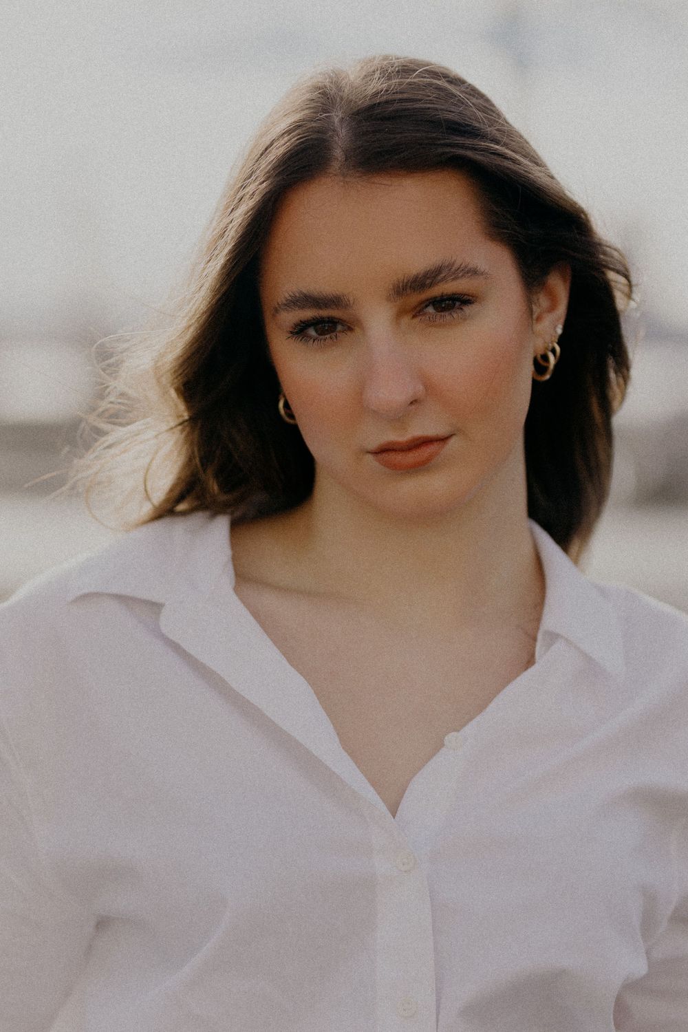 Close-up portrait shot with soft lighting highlighting natural makeup and a white collared shirt.