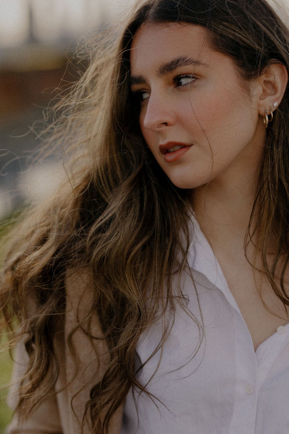 Side-angle portrait with wavy hair and red lipstick against a soft background.