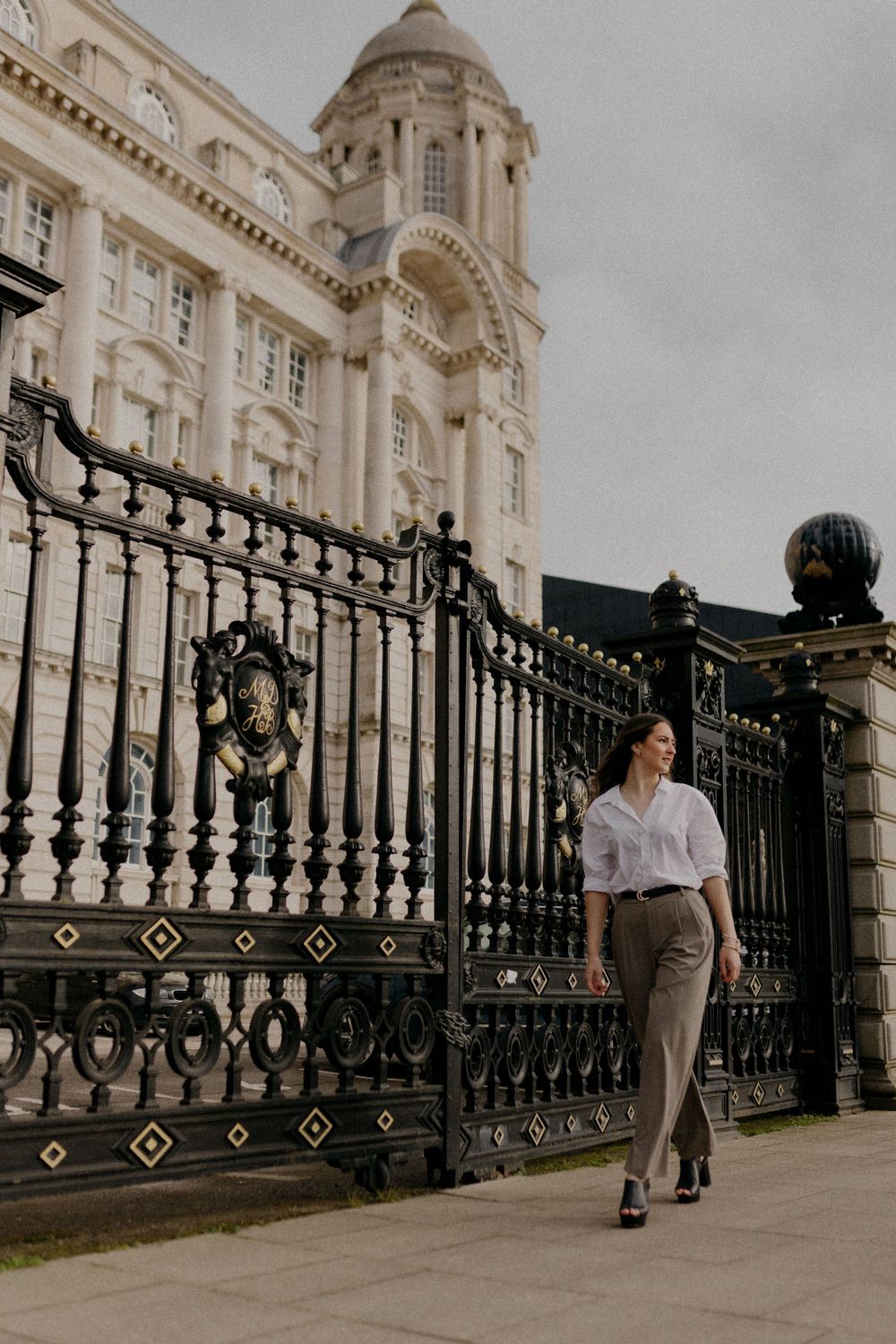 Person walks past ornate iron gates of grand historic building.