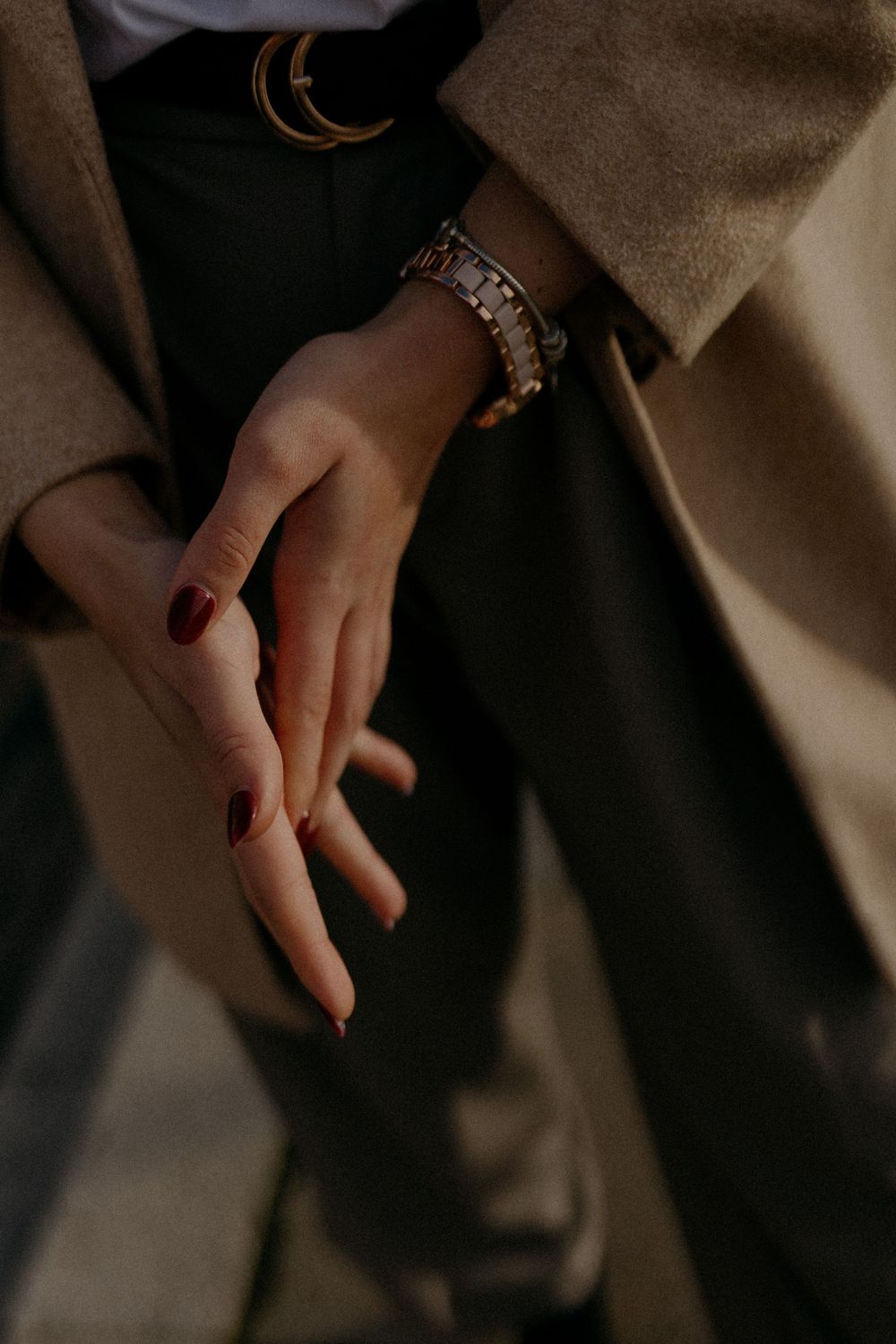 Close-up of hands with red nail polish and jewelry against a dark background.