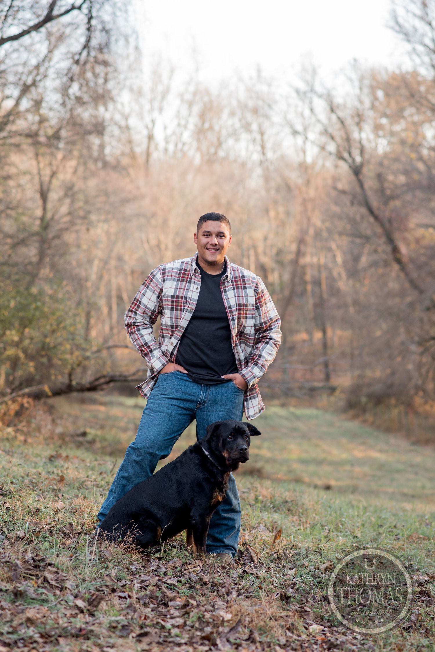 Person in plaid flannel posing with black dog in autumn woodland setting.