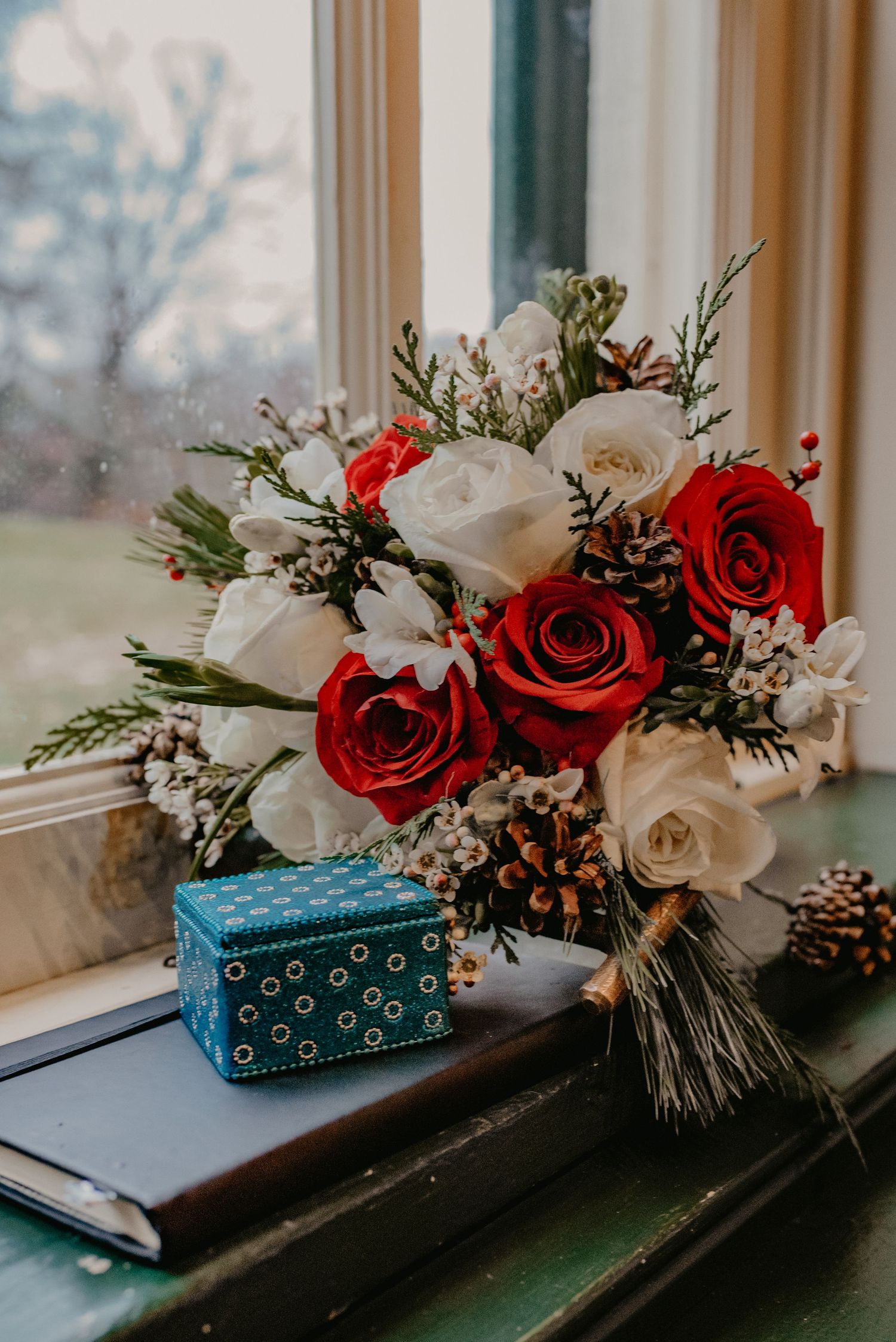 Elegant floral arrangement with red and white roses sits on a windowsill beside a teal gift box.