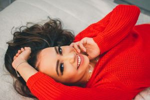Woman in bright red sweater relaxes on white bedding with playful expressions.
