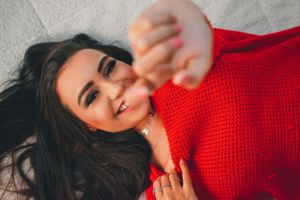 Person in red sweater lying down with dark hair smiling warmly against blurred background.
