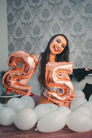 25th birthday celebration with rose gold number balloons and white decorative balloons against damask wallpaper.
