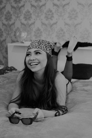 Black and white portrait with leopard print headband and sunglasses on soft bedding.