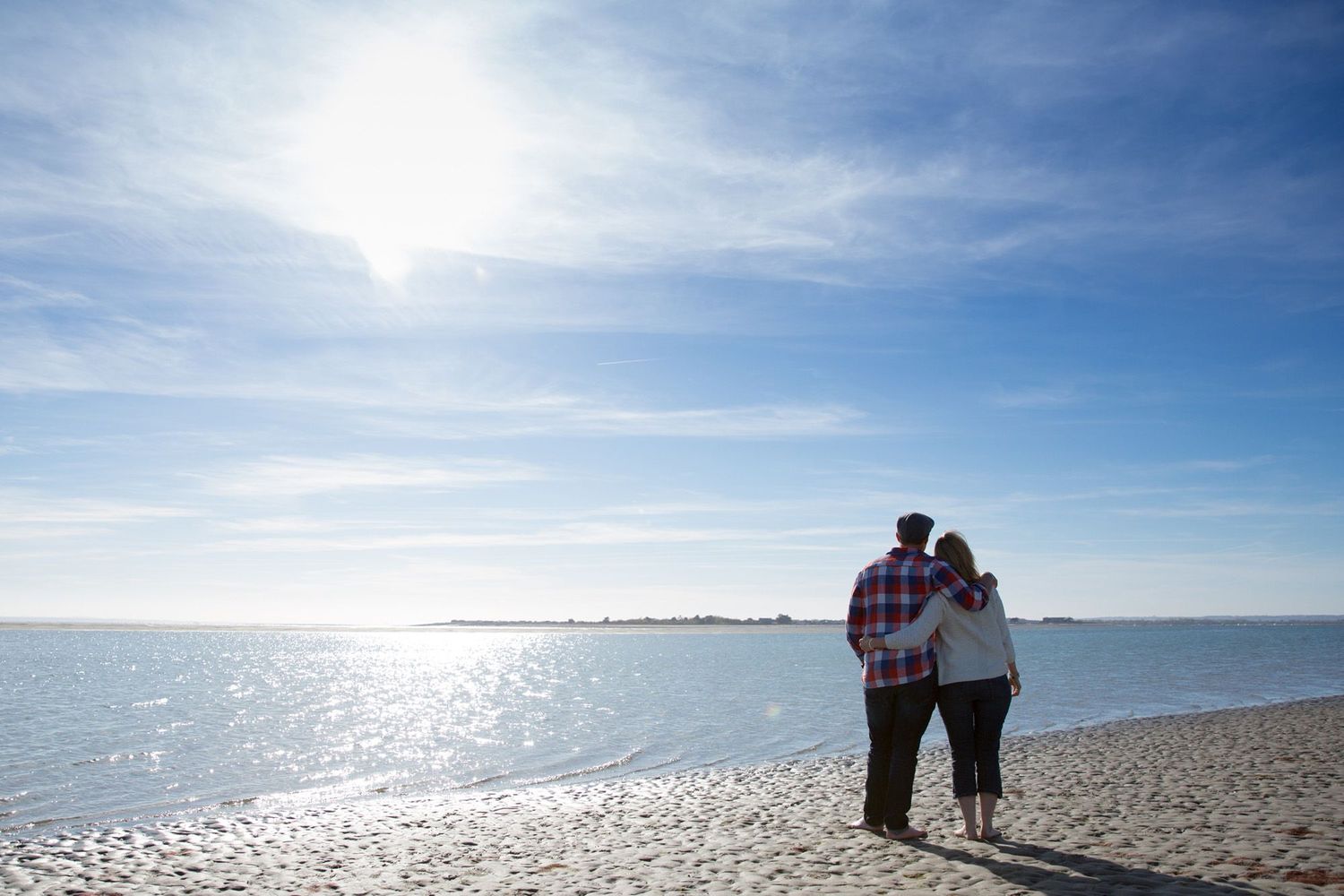 Two people stand together watching the sunset over the ocean on a sandy beach.