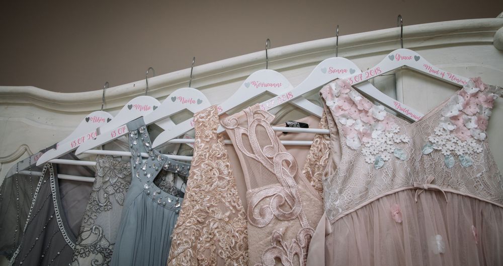 Delicate pastel bridesmaid dresses hanging on white hangers displaying various lace and floral details.