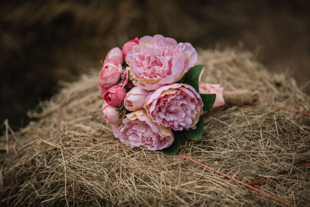 Pink peony bridal bouquet resting on rustic hay bale.