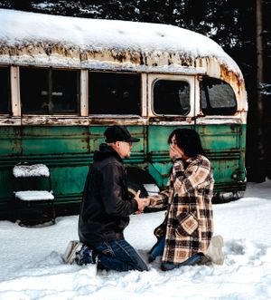 A winter proposal scene with a snow-covered vintage bus in the background.