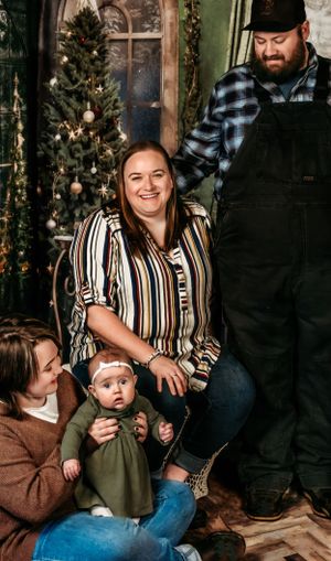A family poses in a festive holiday setting with a decorated Christmas tree and vintage arched window in the background.