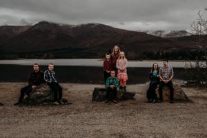 A moody landscape photo of a gathering by a lake with mountains and dark clouds in the background.