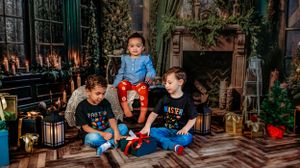 Holiday photo scene with kids sitting on wooden floor surrounded by Christmas decorations and lanterns.