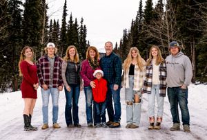 A family portrait in winter with evergreen trees and snow in the background.