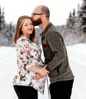 Romantic winter portrait of a couple embracing on a snow-covered trail with evergreen forest background.