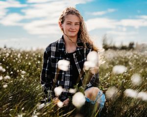 Someone in a plaid shirt sitting among cotton plants in a sunny field.
