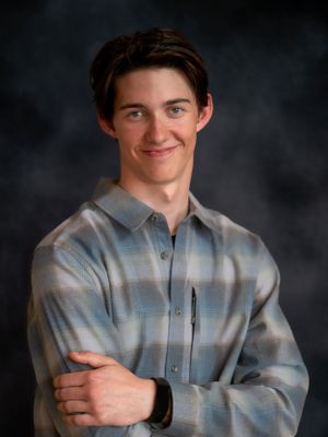 Studio portrait featuring a person in a plaid shirt with crossed arms and slight smile.