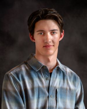 Portrait of a young person in a plaid button-up shirt against a dark studio background.