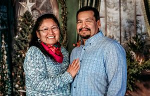 Couple posing together in front of Christmas themed backdrop with decorative elements.