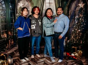 Family holiday portrait with Christmas trees and decorative lighting in background.