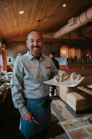 Restaurant worker in uniform holding a serving tray with food items.