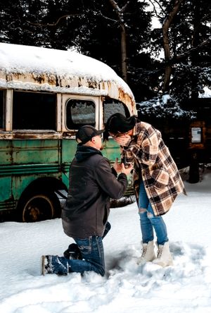 A romantic proposal scene in the snow beside a vintage green bus.
