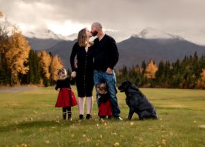 A family portrait with children and their black dog against a mountain landscape with fall colors.