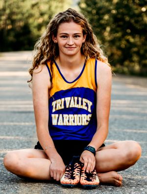 An athlete wearing a Tri Valley Warriors yellow and blue jersey sitting cross-legged outdoors.