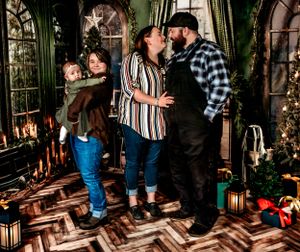 Holiday family portrait in a cozy room with herringbone floors, Christmas trees and glowing lanterns.