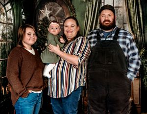 Family group portrait in rustic holiday setting with Christmas decorations and twinkling lights.