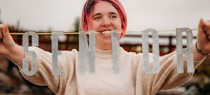 Person in neutral sweater stretches arms wide against industrial background.