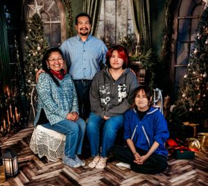 Family portrait in front of Christmas trees with vintage-style holiday decorations.