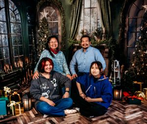 Family group photo in festive holiday setting with Christmas trees and twinkling lights.