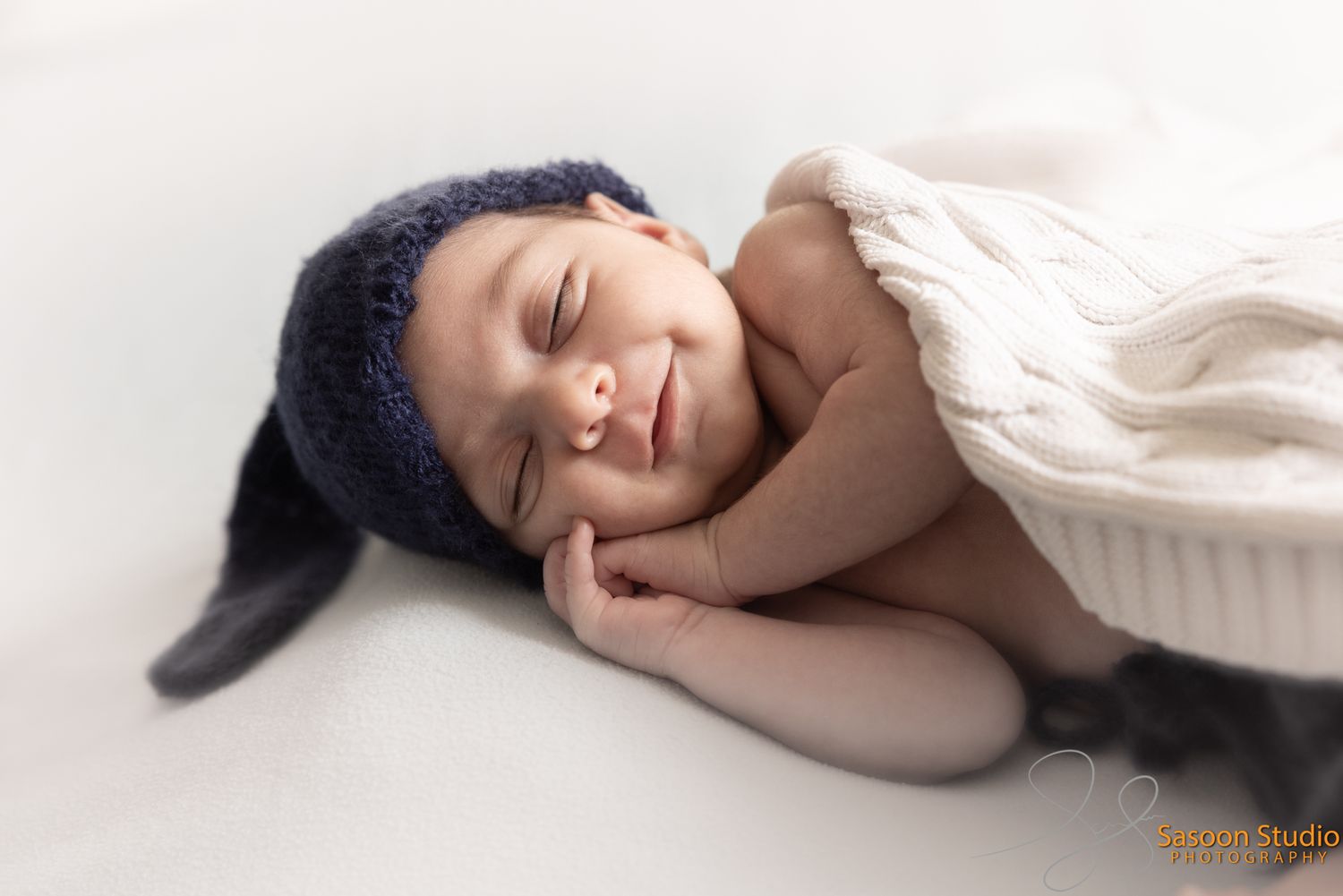 Baby wrapped in white blanket sleeping peacefully while wearing dark blue knit hat.