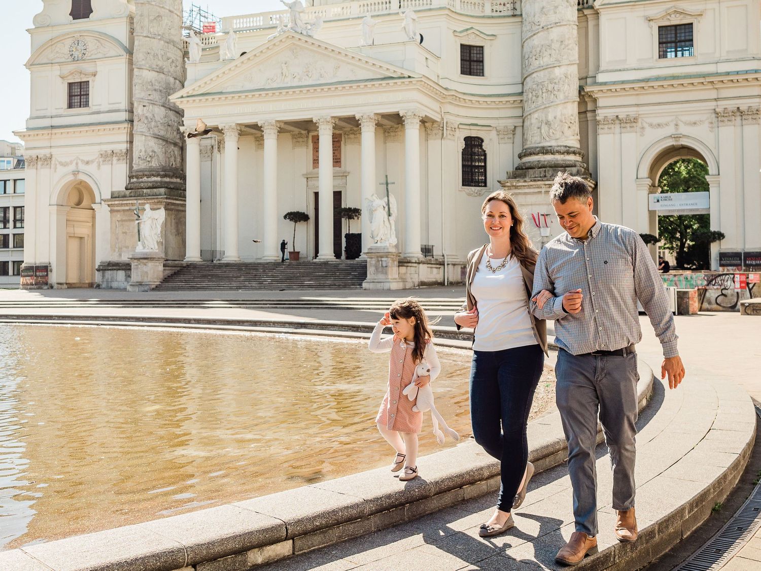 Family of three with toddler walking next to fountain in Central Europe