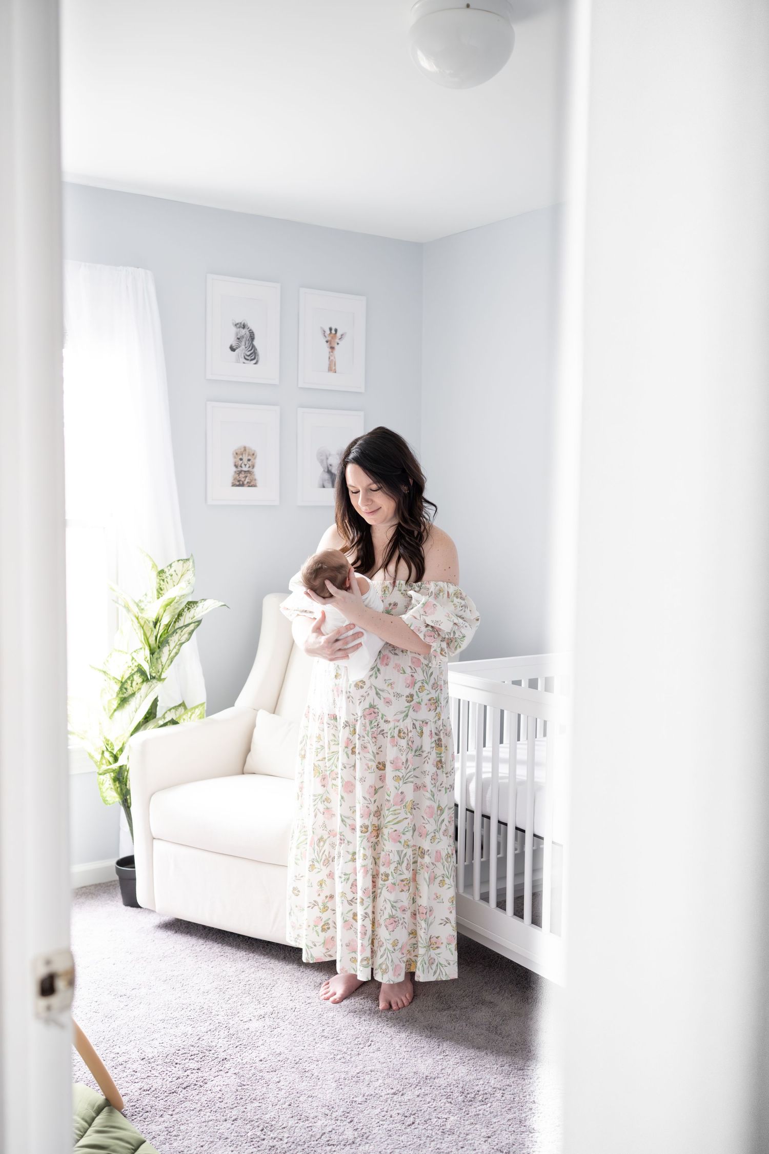 zoomed out image of mom in baby's nursery.  she is holding baby boy in her arms and staring lovingly down at him